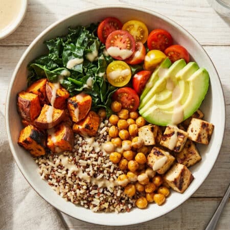 Un bol coloré composé de quinoa, pois chiches, tofu, patates douces, avocat, tomates cerises et chou kale.