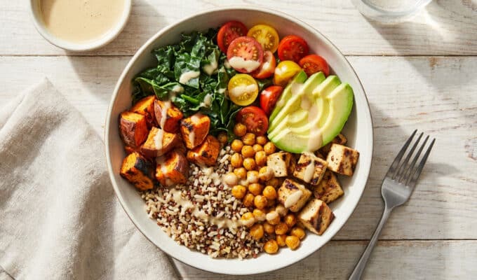 Un bol coloré composé de quinoa, pois chiches, tofu, patates douces, avocat, tomates cerises et chou kale.