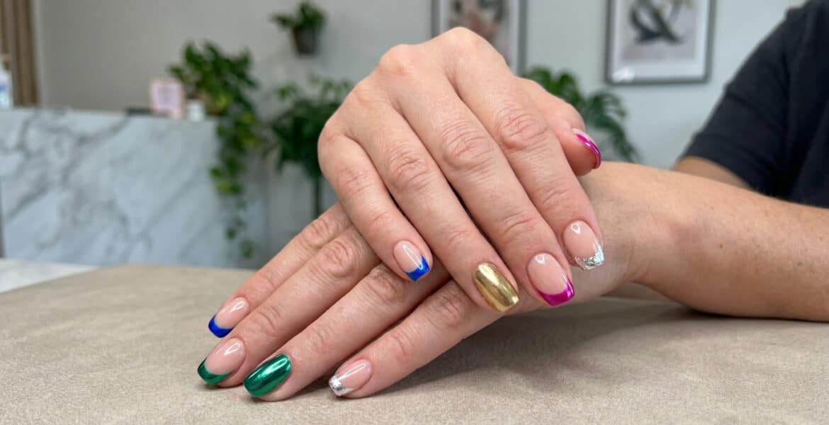 Mains avec une french manucure aux bouts colorés et métallisés, et un ongle entièrement doré.