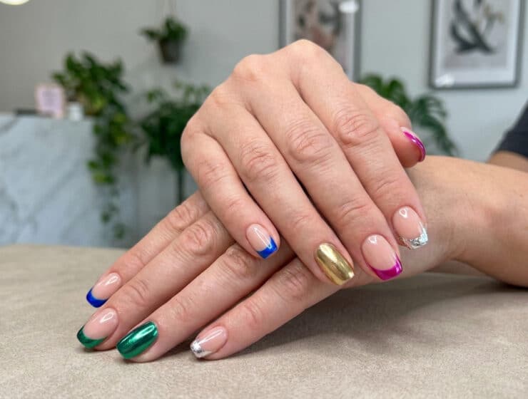 Mains avec une french manucure aux bouts colorés et métallisés, et un ongle entièrement doré.