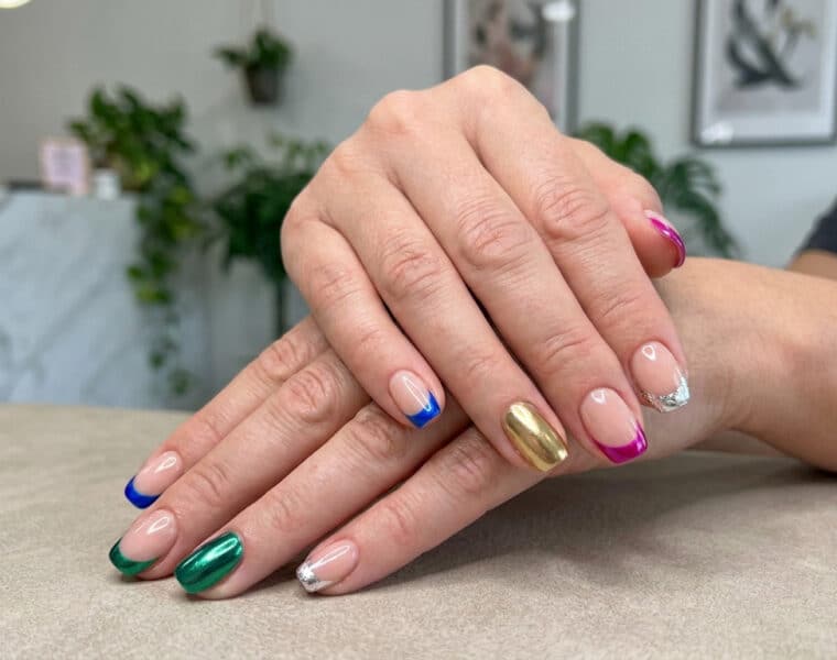 Mains avec une french manucure aux bouts colorés et métallisés, et un ongle entièrement doré.
