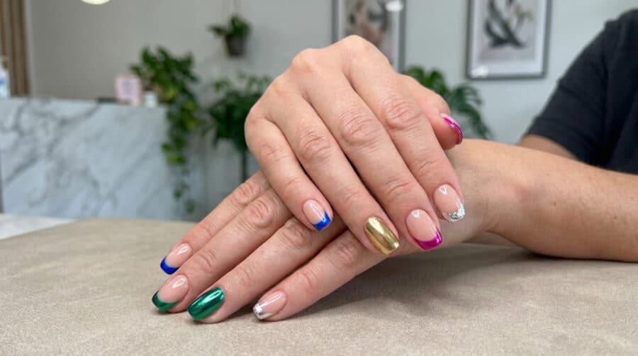 Mains avec une french manucure aux bouts colorés et métallisés, et un ongle entièrement doré.