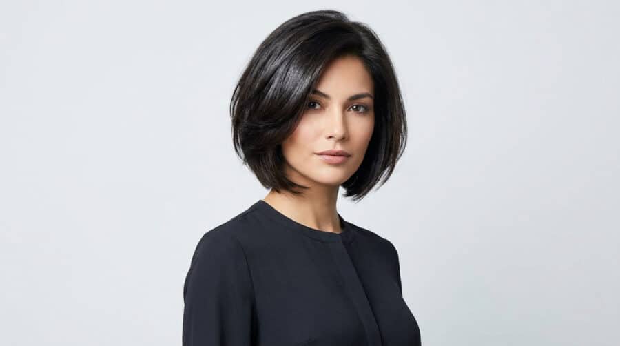 Portrait d'une femme aux cheveux bruns avec une coupe au carré plongeant volumineuse sur fond gris clair.