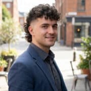 Homme aux cheveux bouclés avec une coupe mulet moderne portant un blazer bleu dans une rue citadine.
