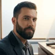 Un homme élégant avec une barbe courte bien taillée, posant dans une salle de bain moderne avec une tondeuse.