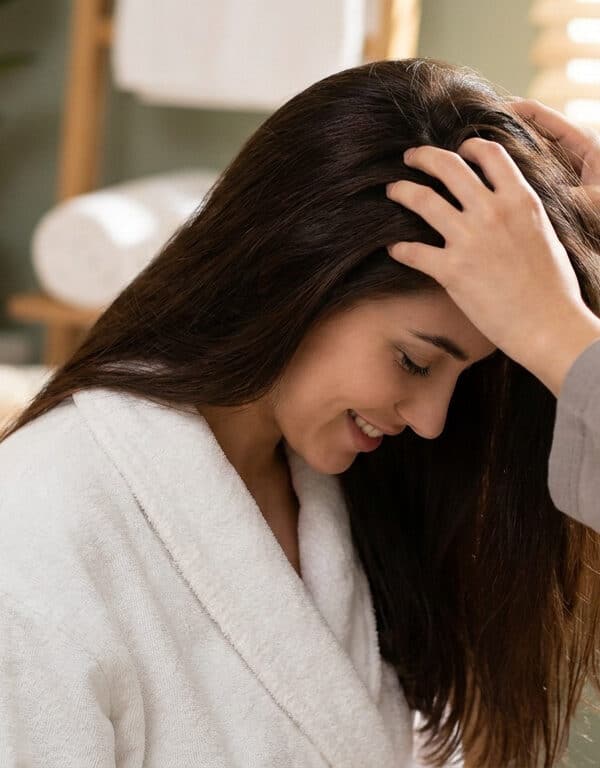 Femme en peignoir recevant un massage du cuir chevelu relaxant dans un spa.