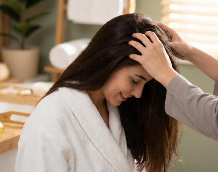 Femme en peignoir recevant un massage du cuir chevelu relaxant dans un spa.