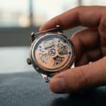 Gros plan sur le fond transparent d'une montre automatique tenue par une main, révélant le mouvement complexe.