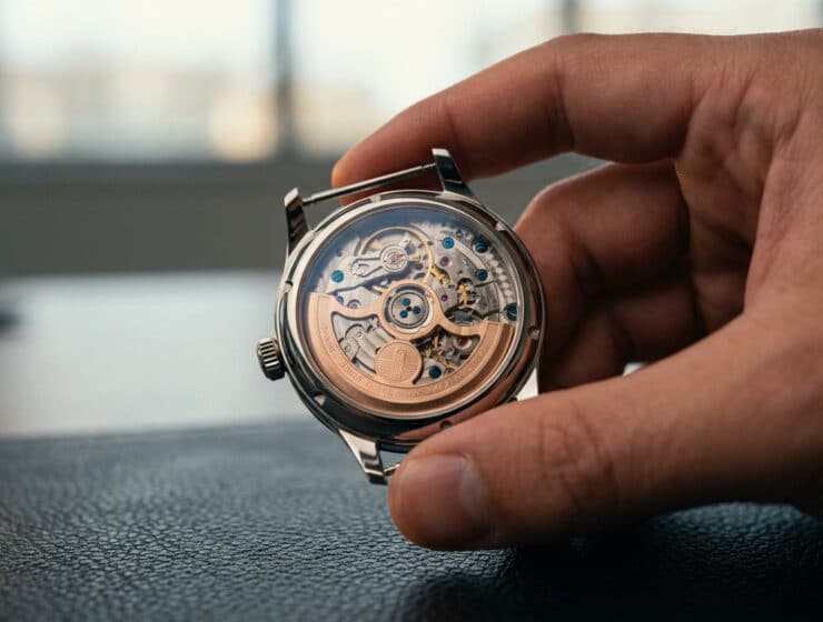 Gros plan sur le fond transparent d'une montre automatique tenue par une main, révélant le mouvement complexe.