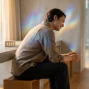 Un homme souriant assis devant une horloge numérique affichant 11:11 avec des reflets arc-en-ciel sur le mur.