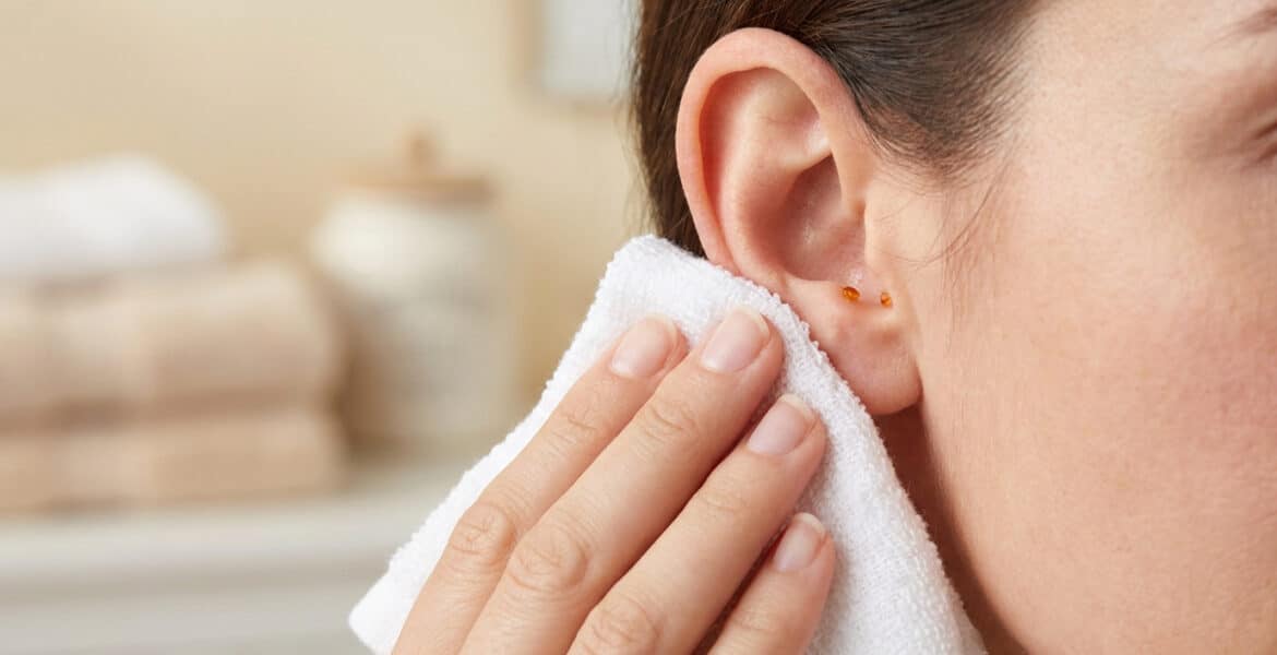 Une femme essuie délicatement l'extérieur de son oreille avec une serviette blanche propre dans une salle de bain.
