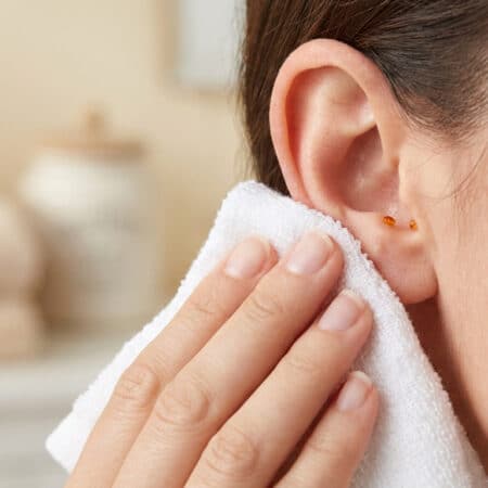 Une femme essuie délicatement l'extérieur de son oreille avec une serviette blanche propre dans une salle de bain.