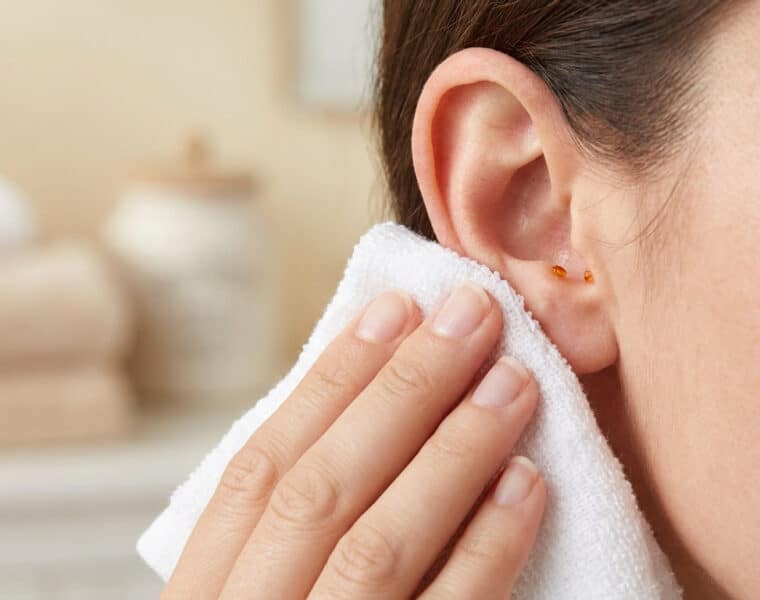 Une femme essuie délicatement l'extérieur de son oreille avec une serviette blanche propre dans une salle de bain.
