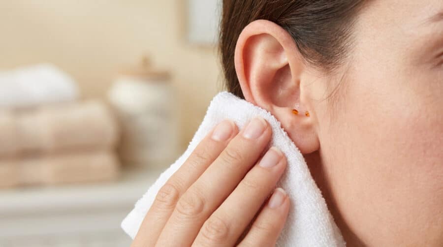 Une femme essuie délicatement l'extérieur de son oreille avec une serviette blanche propre dans une salle de bain.