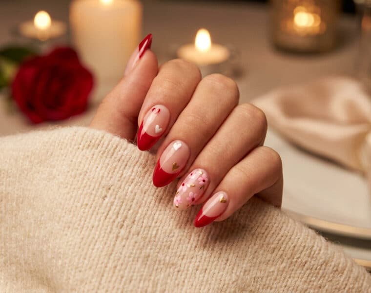 Une main portant un pull beige avec des ongles en amande décorés de motifs rouges, cœurs et fleurs pour la Saint-Valentin.