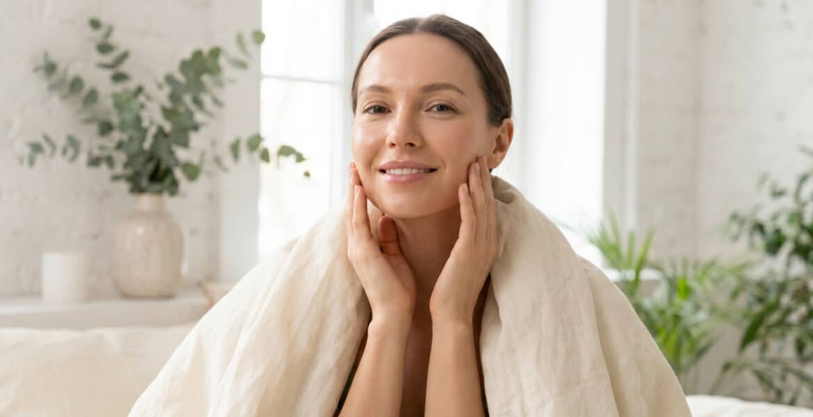 Une femme souriante s'effleurant le visage dans une pièce lumineuse pour un drainage lymphatique naturel.