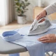 Une personne repasse une chemise bleue claire sur une planche à repasser avec un fer à vapeur.