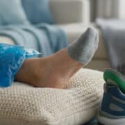 Un pied reposant sur un coussin avec une poche de glace bleue, une chaussure de sport avec semelle orthopédique à côté.