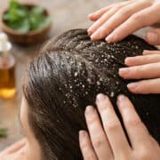 Mains massant un cuir chevelu avec un gommage au sel exfoliant près d'ingrédients naturels.