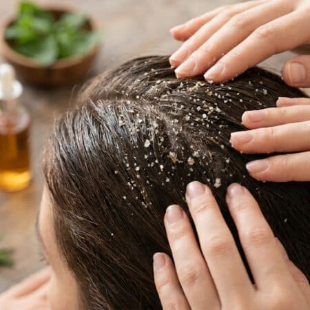 Mains massant un cuir chevelu avec un gommage au sel exfoliant près d'ingrédients naturels.