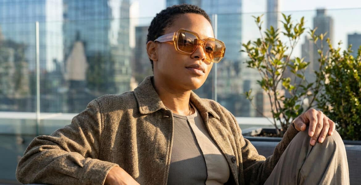 Femme portant des lunettes de soleil oversize ambrées sur un rooftop urbain.