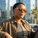 Femme portant des lunettes de soleil oversize ambrées sur un rooftop urbain.