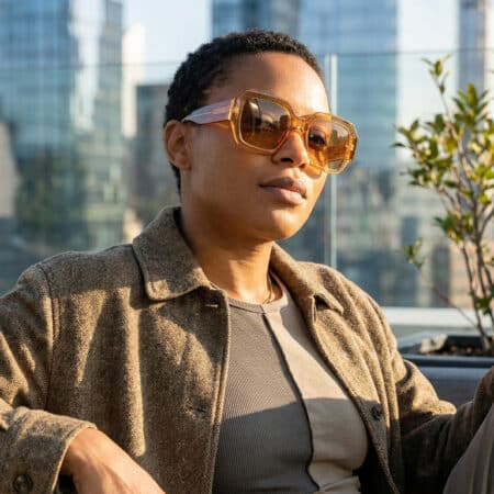 Femme portant des lunettes de soleil oversize ambrées sur un rooftop urbain.