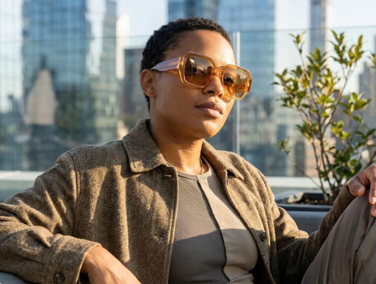 Femme portant des lunettes de soleil oversize ambrées sur un rooftop urbain.