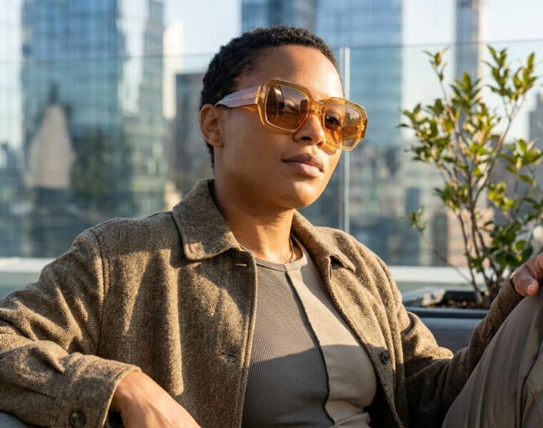 Femme portant des lunettes de soleil oversize ambrées sur un rooftop urbain.