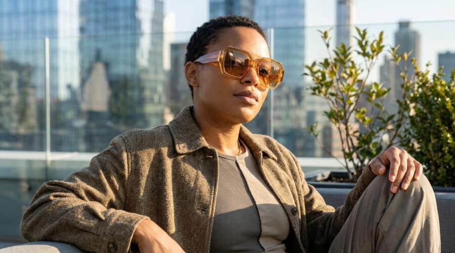 Femme portant des lunettes de soleil oversize ambrées sur un rooftop urbain.
